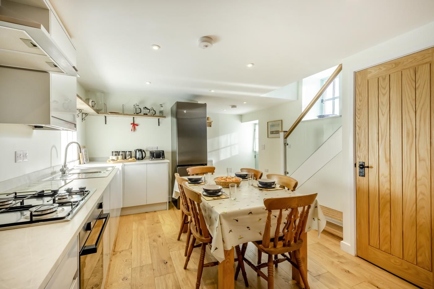 A modern kitchen with a dining area, wooden flooring, and a staircase leading to an upper level.