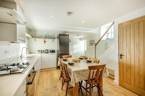 A modern kitchen with a dining area, wooden flooring, and a staircase leading to an upper level.
