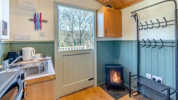 A compact kitchen with a wood stove, a sink, and a window overlooking trees. - 1 Bed in Lanercost (oc-t35009) (Burtholme)