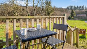 An outdoor seating area with a table and chairs, a wooden deck, and a view of a grassy field and trees. - 1 Bed in Lanercost (oc-t35009) (Burtholme)