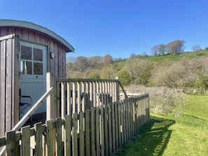 A wooden cabin with a curved roof, a wooden fence, and a grassy yard.