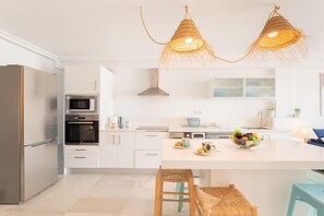 A modern kitchen with white cabinetry, stainless steel appliances, a central island with stools, and a hanging light fixture. - Coastal Escape with Private Pool for 6 (San José)