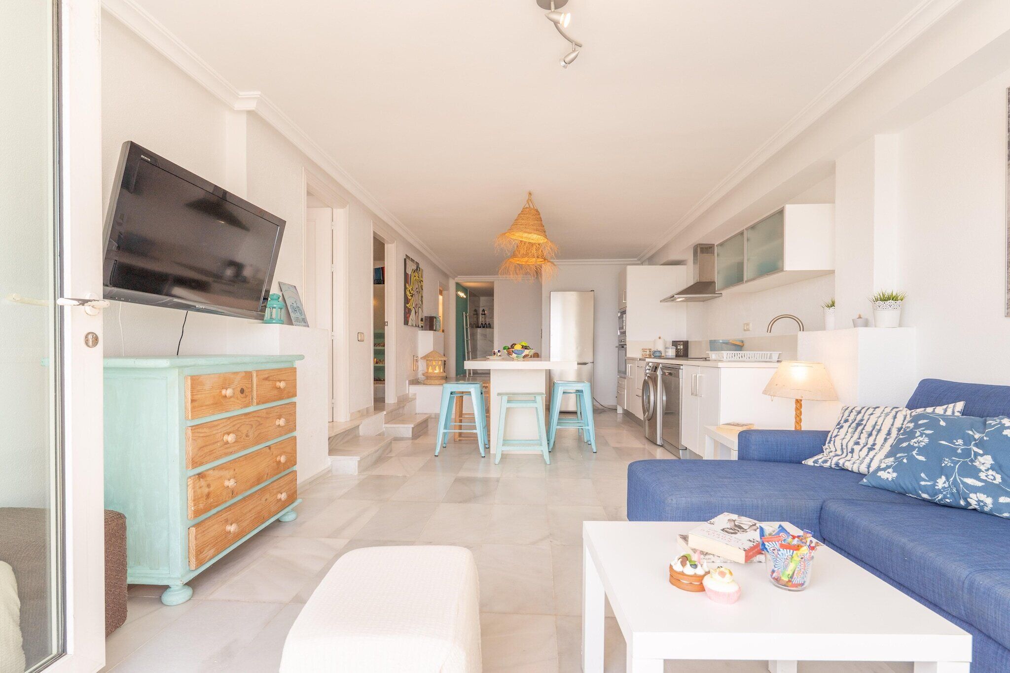 Un saló modern amb un sofà, una televisió, una zona de menjador i una cuina.