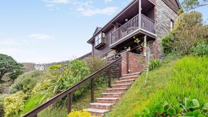 Ein Haus mit einer Holztreppe, die zu einem Balkon führt, umgeben von üppigem Grün.
