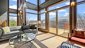 Un interior moderno con sofá, mesa de centro y sillas, ventanas amplias y un balcón.