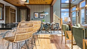 Un interior espacioso con techo de madera, ventanas amplias, mobiliario de mimbre y una escalera.