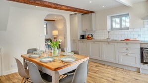 Eine moderne Küche mit weißen Schränken, einem Holztisch für vier Personen und einem sichtbaren Backofen.
