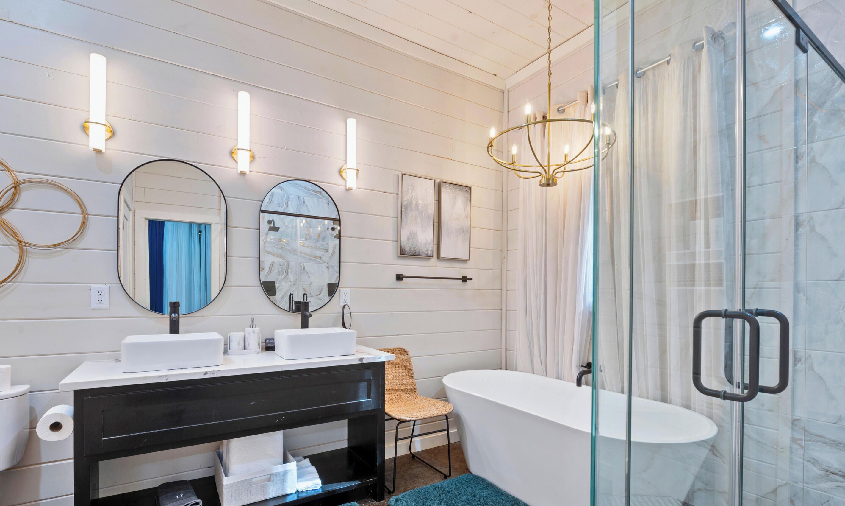 Ein modernes Badezimmer mit einer freistehenden Badewanne, zwei wandmontierten Waschbecken, einem großen Spiegel und einer Chandelier.