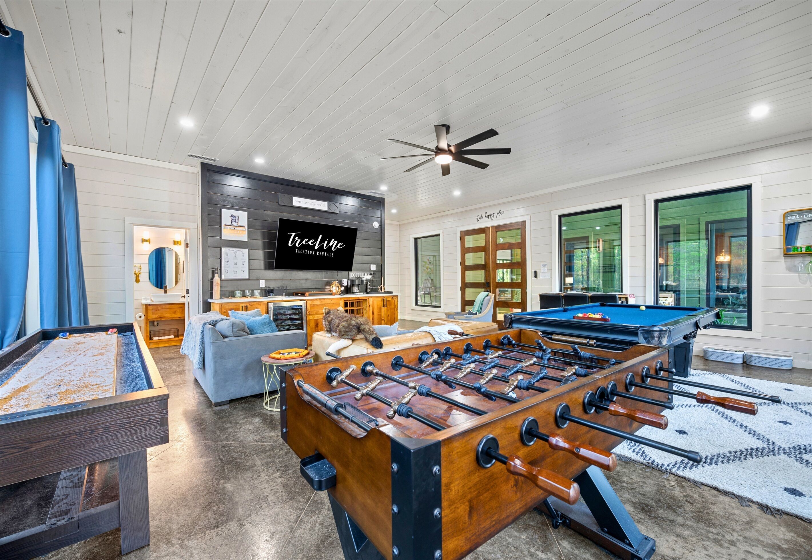 A spacious living area with a foosball table, a pool table, and a cozy seating area with a sofa and a cat.