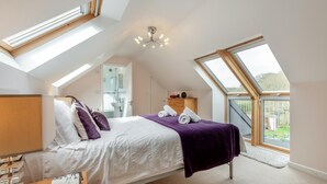 Un dormitorio con tragaluz, una cama con manta púrpura, una mesita de noche y vistas al exterior.