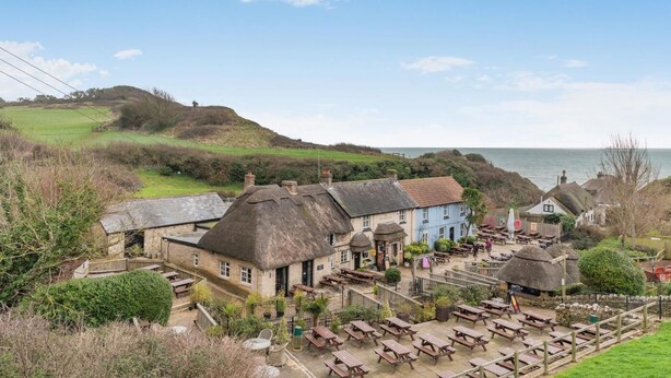 Un pueblo costero con edificios de piedra tradicionales, un pub con techo de paja y terraza al mar.