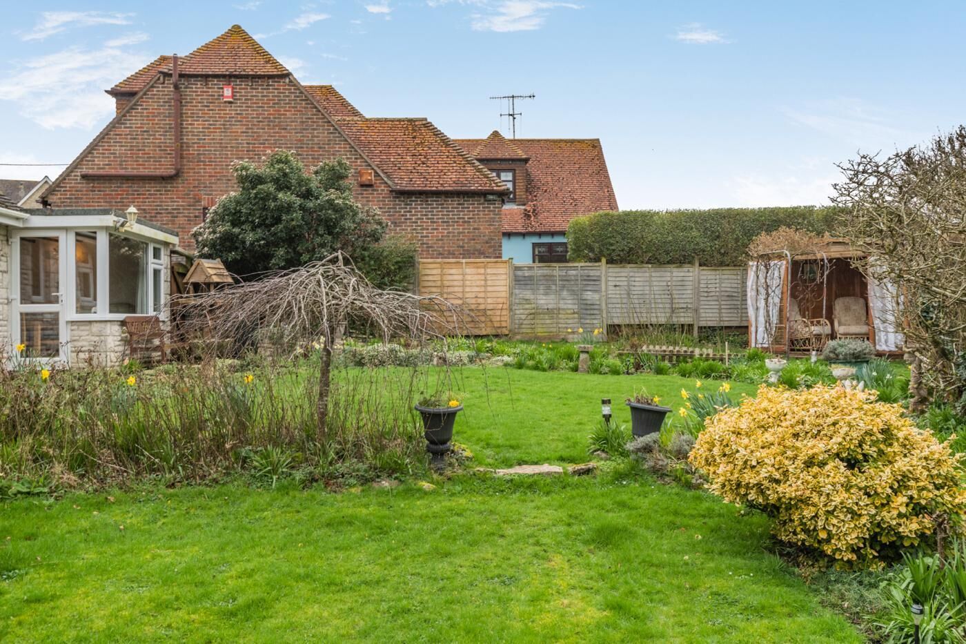 A brick house with a sloped roof, a garden with grass and plants, and a wooden fence.