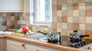 Una cocina con salpicadero de azulejos, una estufa, una olla y verduras sobre la encimera.
