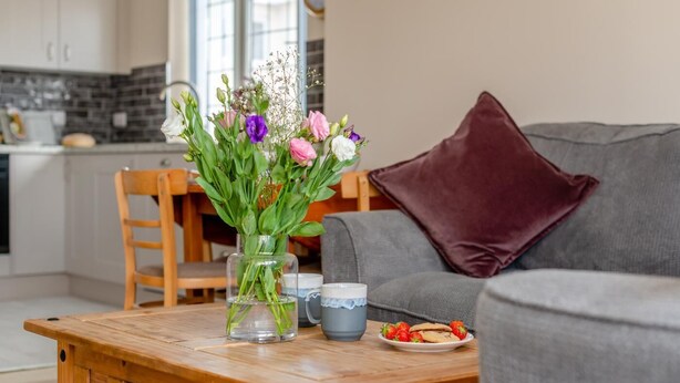 Ett träbord med en vas med blommor, en tallrik med jordgubbar och en mugg.
