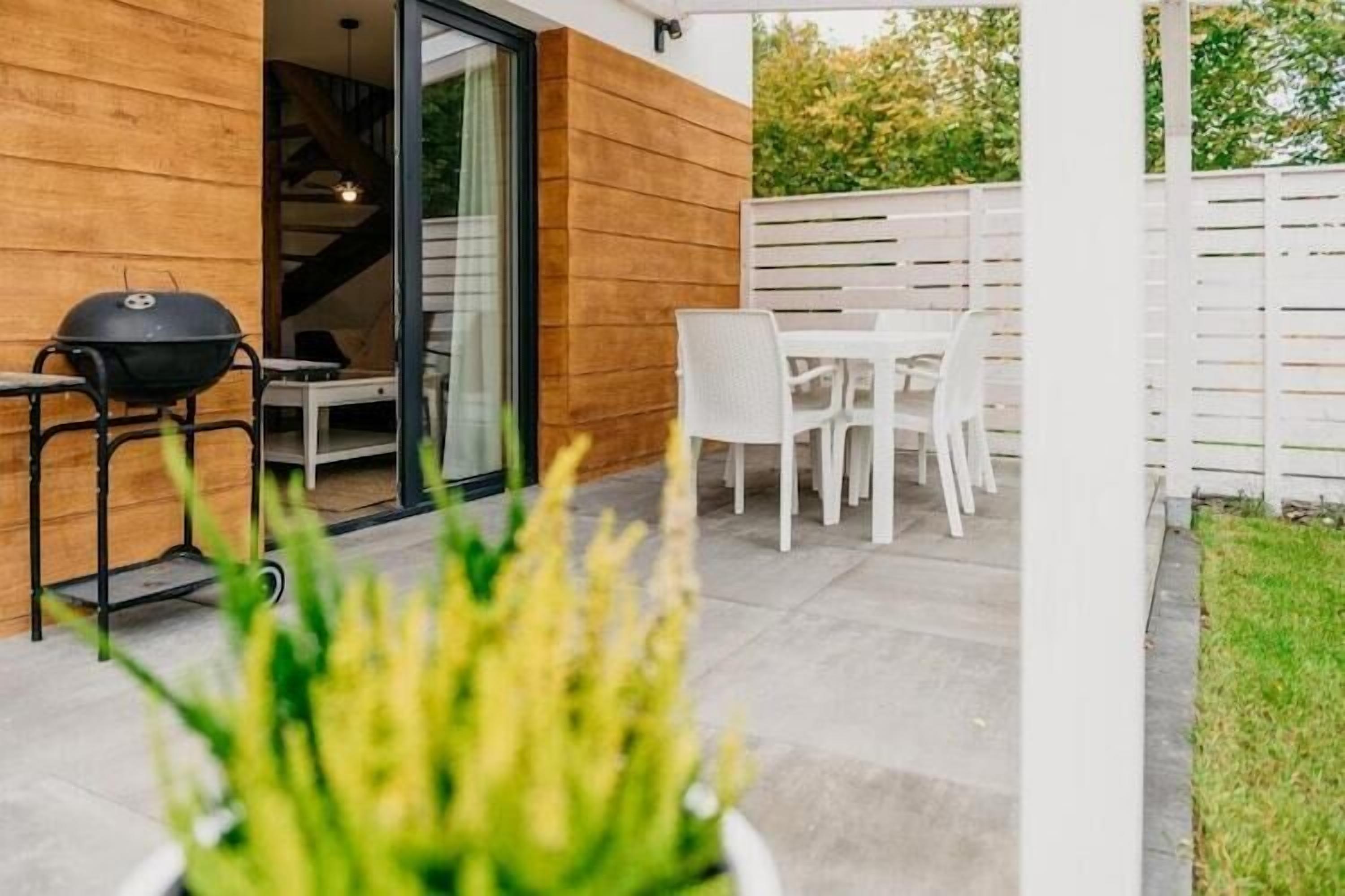 Une terrasse avec un barbecue, des chaises blanches et une table.