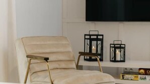 A beige chair with gold legs, a black TV on the wall, and two black candle holders with candles. - Comfortable holiday home, sauna, jacuzzi (Kopalino)