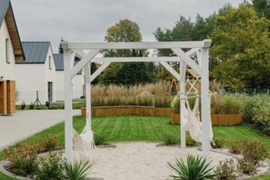 Eine weiße Pergola in einem Garten mit Rasen, einer Schaukel und einem Holzzaun im Hintergrund.