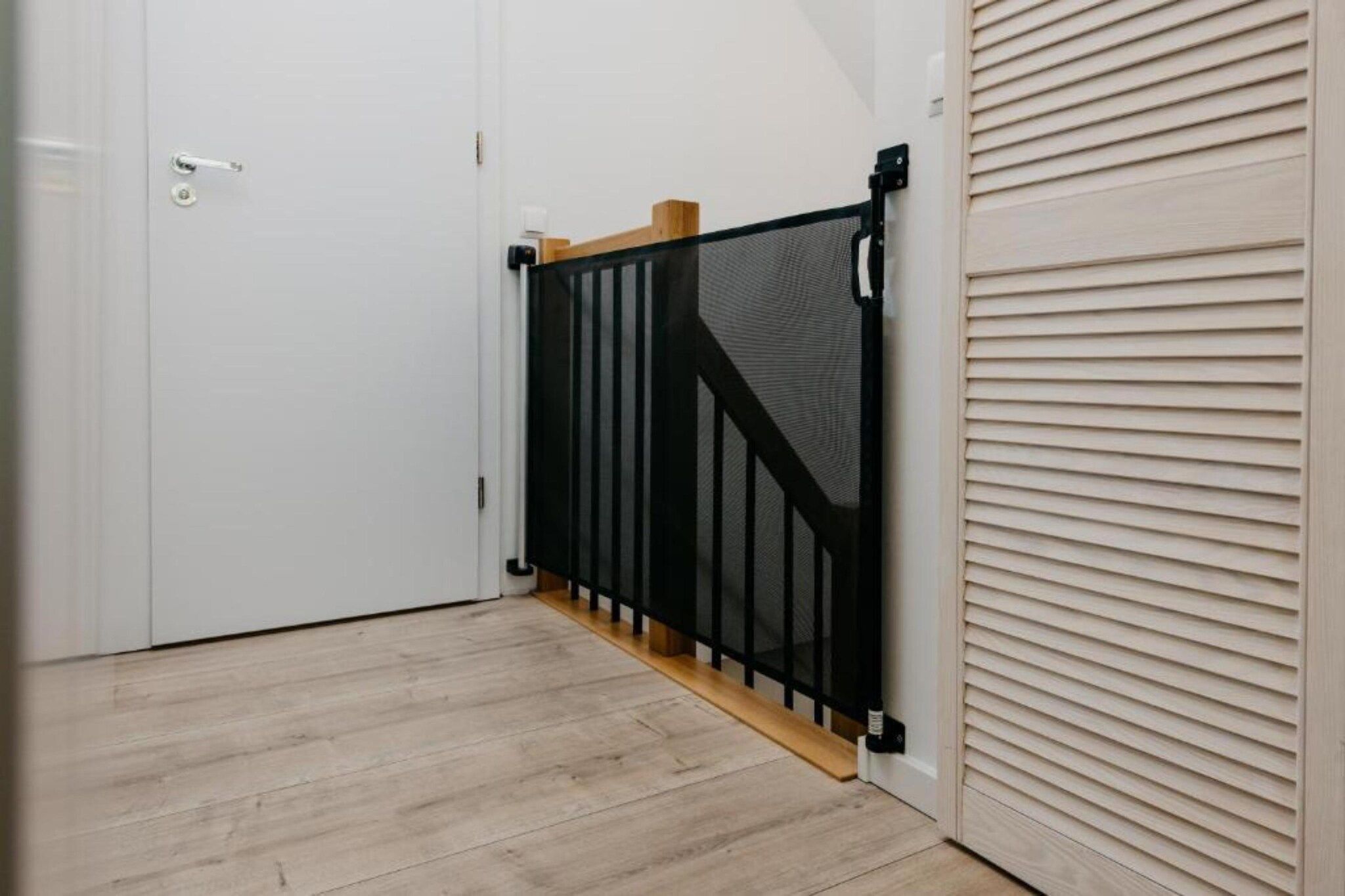 Een kamer met een witte deur, een zwart metalen hekwerk en een houten vloer.