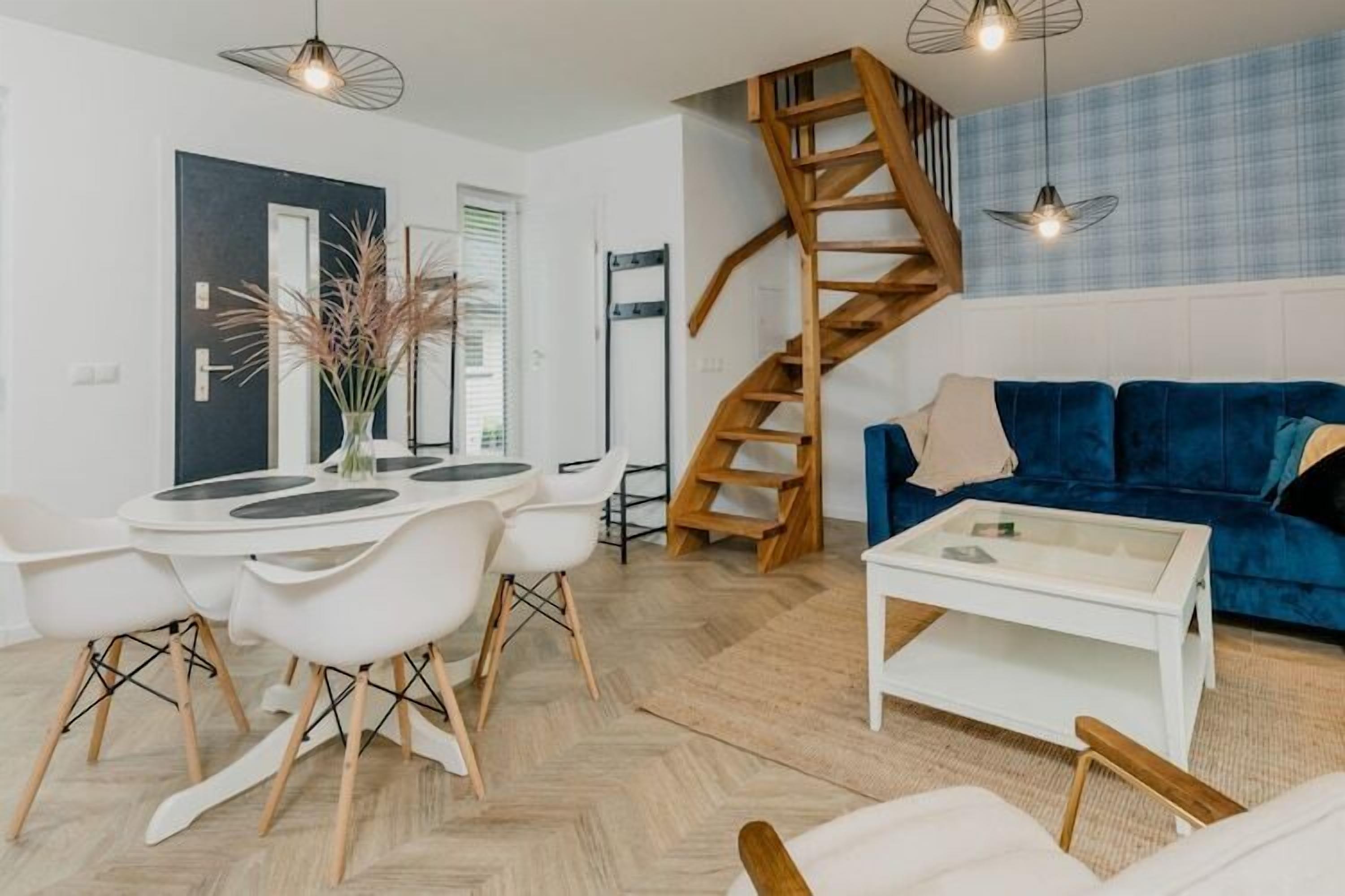 Un salon moderne avec un canapé bleu, des chaises blanches, une table à manger et un escalier en bois.