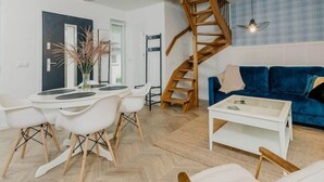 A modern living room with a blue sofa, white chairs, a dining table, and a wooden staircase. - Comfortable holiday home, sauna, jacuzzi (Kopalino)