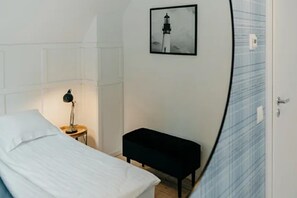 Ein Schlafzimmer mit einem Bett, einem Nachttisch mit Lampe, einer Bank und einem gerahmten Bild an der Wand.
