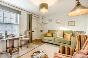 Ein gemütliches Wohnzimmer mit einem Holzesstisch, einem grünen Sofa und einem gestreiften Sessel.