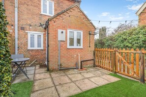 Une maison en briques avec deux fenêtres, une clôture en bois et un petit espace patio.
