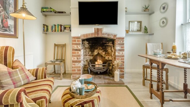 Una sala de estar acogedora con chimenea, un televisor montado encima y un comedor con una mesa dispuesta para una comida.