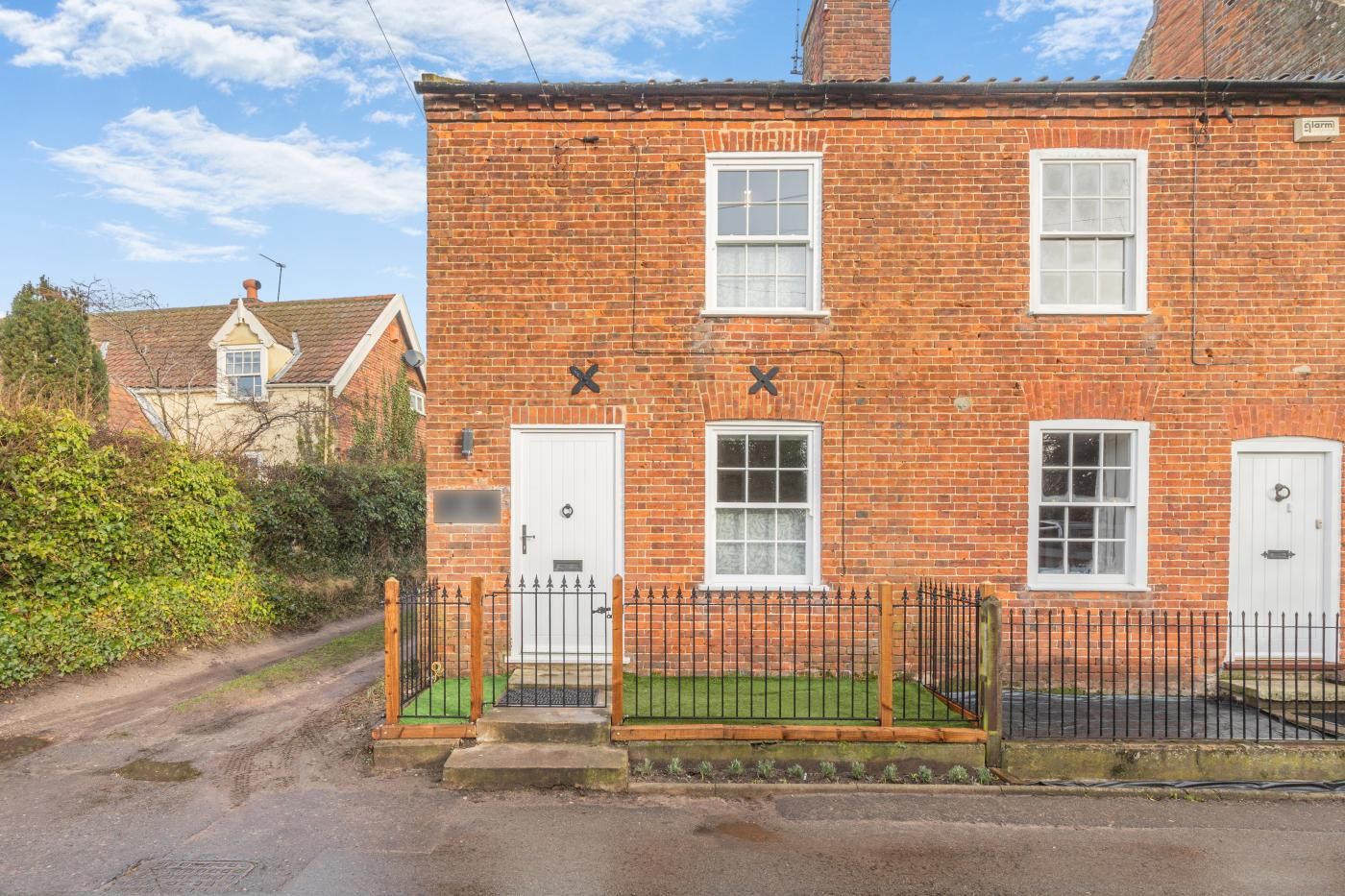 A brick house with a white door, a small porch, and a black metal fence.