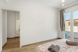 Une chambre d’hôtel avec un plancher en bois, un lit recouvert d’une courtepointe à motifs floraux, un balcon avec vue et une porte donnant sur une autre pièce.