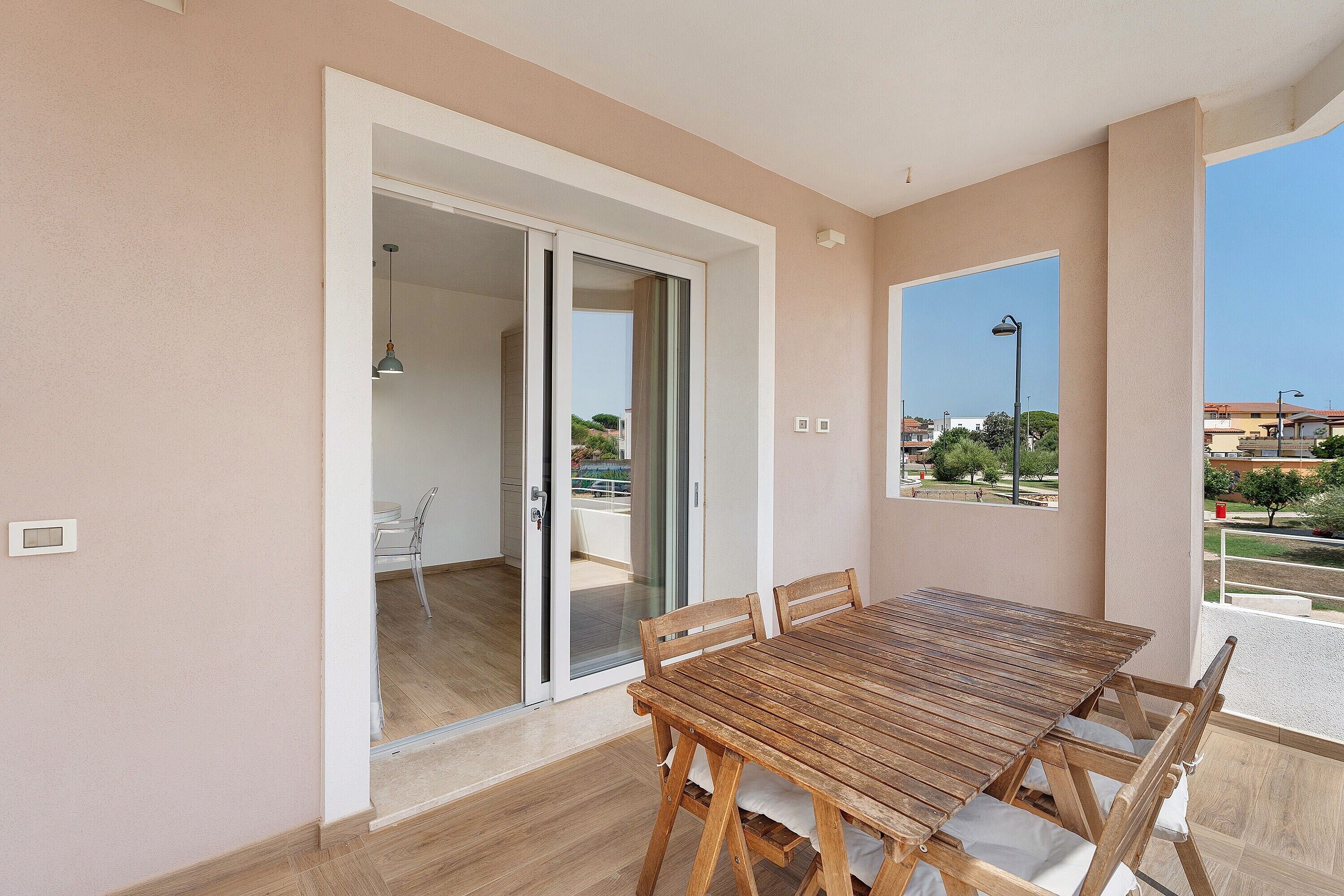 A balcony with a wooden table and chairs, a sliding glass door leading to an indoor space, and a view of the outside.