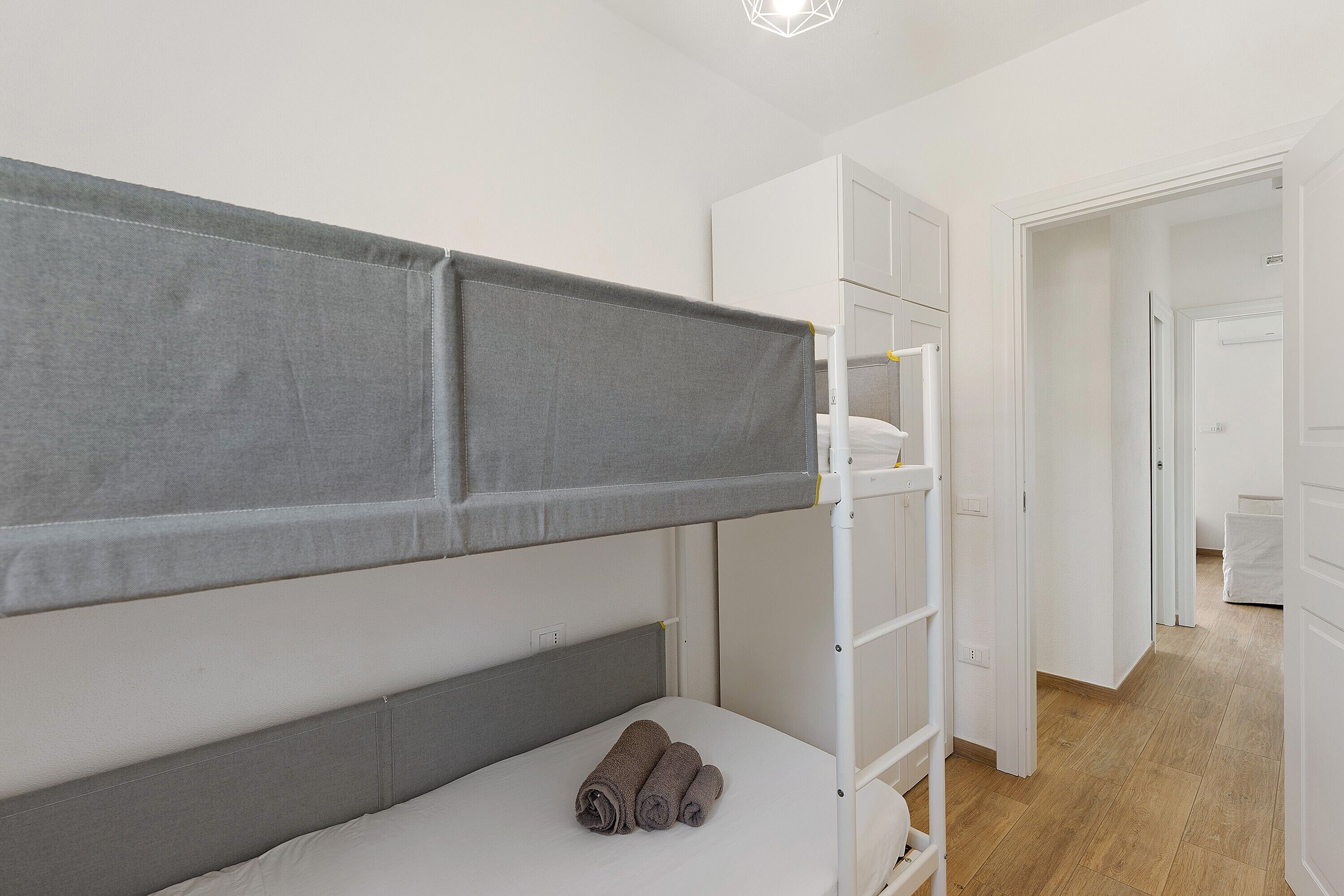 Una habitación con una cama individual superpuesta, un armario blanco y una puerta que da a otra habitación.
