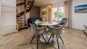 Ein Essbereich mit einem runden Tisch, vier Stühlen, einer Chandelüster, einer Treppe, einem Sofa und Blick ins Freie.