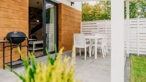Eine Terrasse mit Grill, weißen Stühlen und einem Tisch.