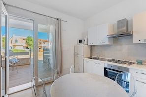 Una cocina moderna con estufa a gas, horno y microondas, un comedor con mesa y sillas, y una puerta corrediza de vidrio que da a un balcón exterior.