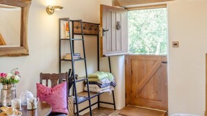A cozy room with a wooden ladder, a door, a small table with a vase of flowers, and a window with a view of trees. - 1 Bed in East Chilla (oc-o34984) (Black Torrington)