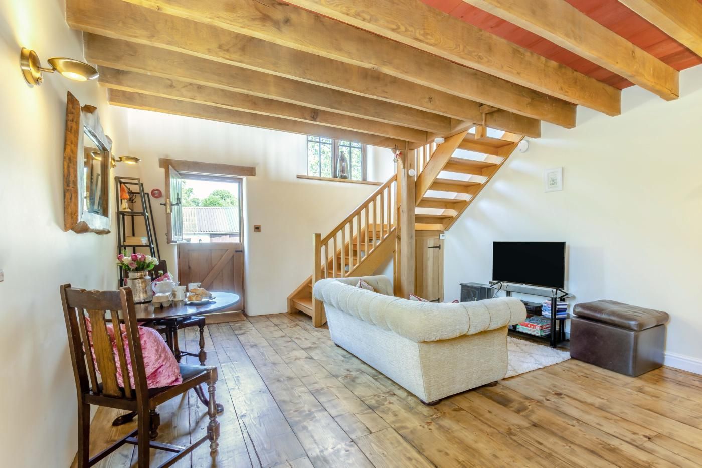 A living room with a wooden floor, a sofa, a television, and a staircase.