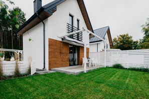 Ein modernes Haus mit weißer Fassade, einer Holz-Akzentwand und einer überdachten Terrasse mit Gartenmöbeln.