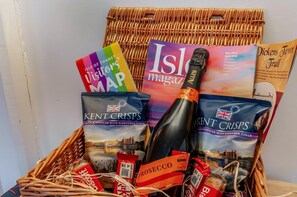 A wicker basket containing Kent Crisp snacks, a bottle of prosecco, and travel brochures. - 3 Bed in Broadstairs (oc-n34799) (Broadstairs)