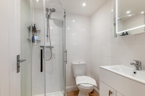 A modern bathroom with a glass shower enclosure, a white toilet, and a sink with a mirror above it. - 3 Bed in Broadstairs (oc-n34799) (Broadstairs)