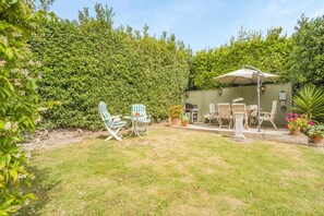 Ein Garten mit einer Terrasse, Gartenmöbeln und einem Grill.