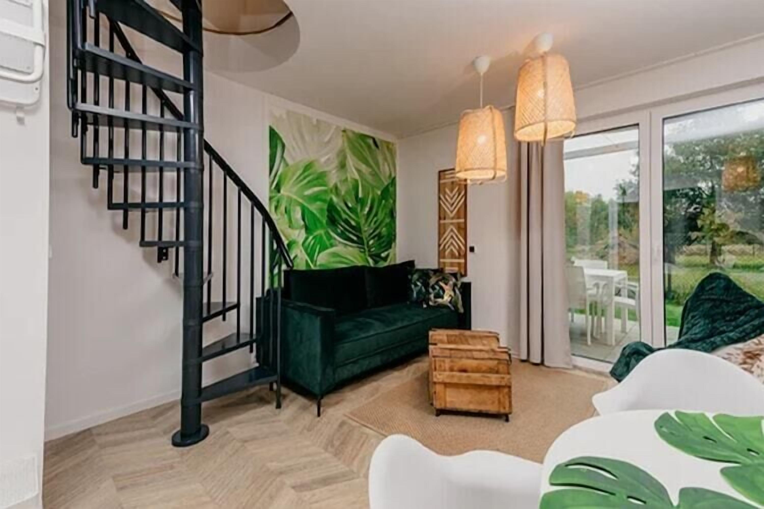 Un intérieur moderne avec un escalier en colimaçon, un canapé vert, une commode en bois et une grande fenêtre donnant sur un paysage verdoyant.