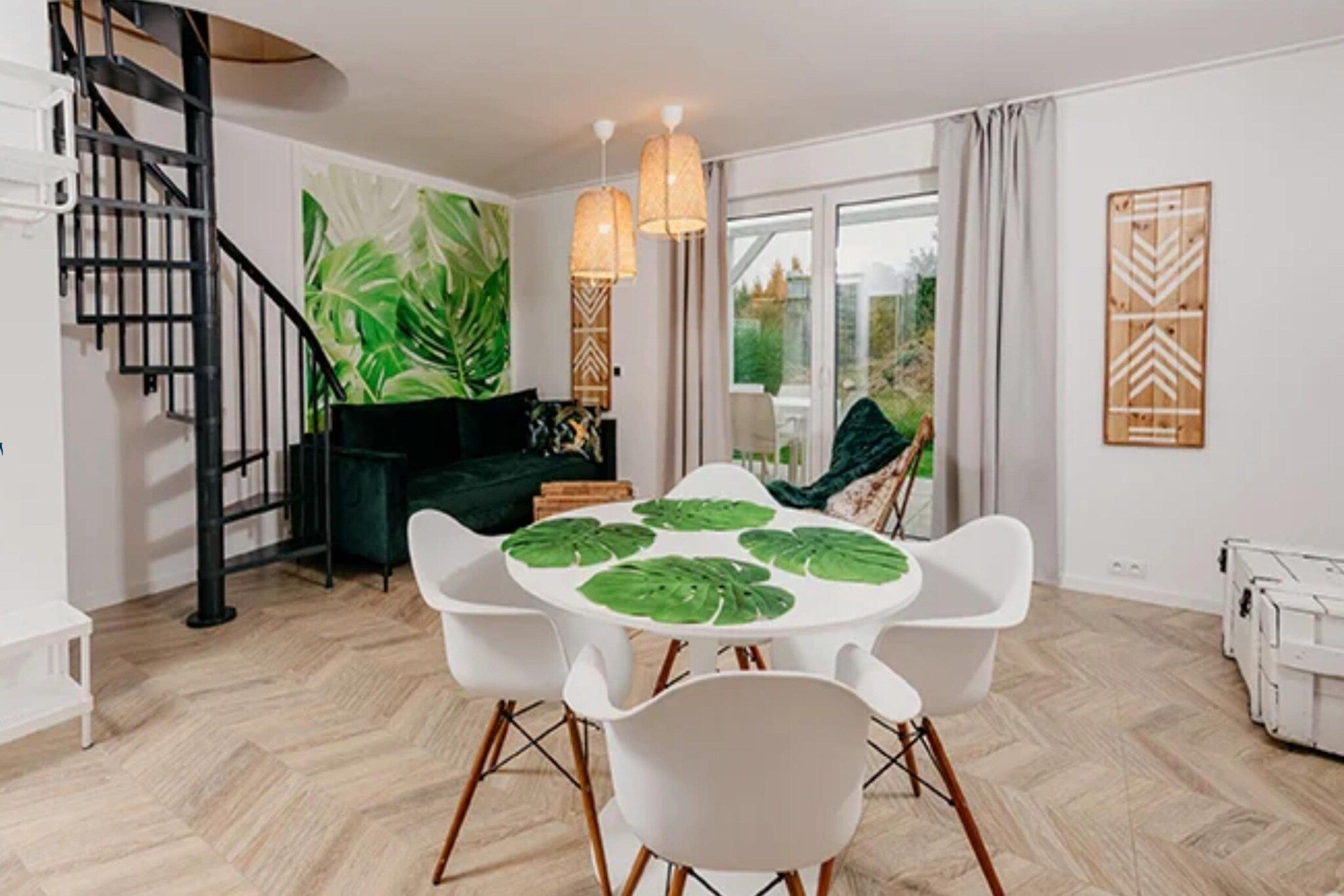 Un comedor moderno con una mesa redonda, sillas blancas y un centro de mesa con follaje verde.
