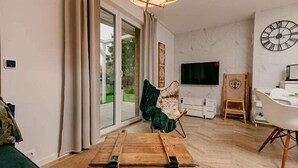 Ein modernes Wohnzimmer mit einer Couch, einer Holzkiste, einem Sessel, einem Esstisch und einem Fernseher.