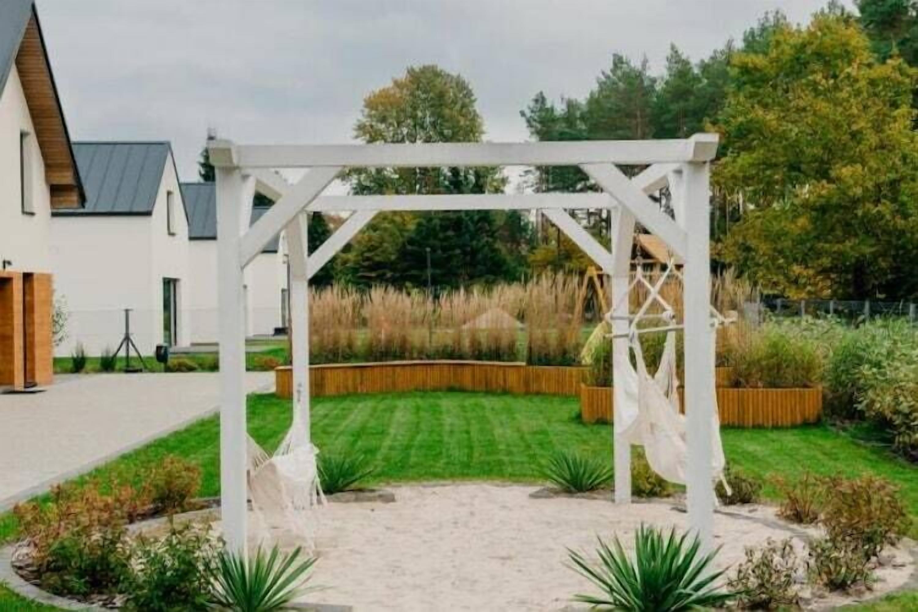 Une pergola blanche dans un jardin, avec une pelouse et des jardinières en bois.