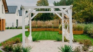 Eine weiße Pergola in einem Garten mit Rasen und Holz-Pflanzkästen.