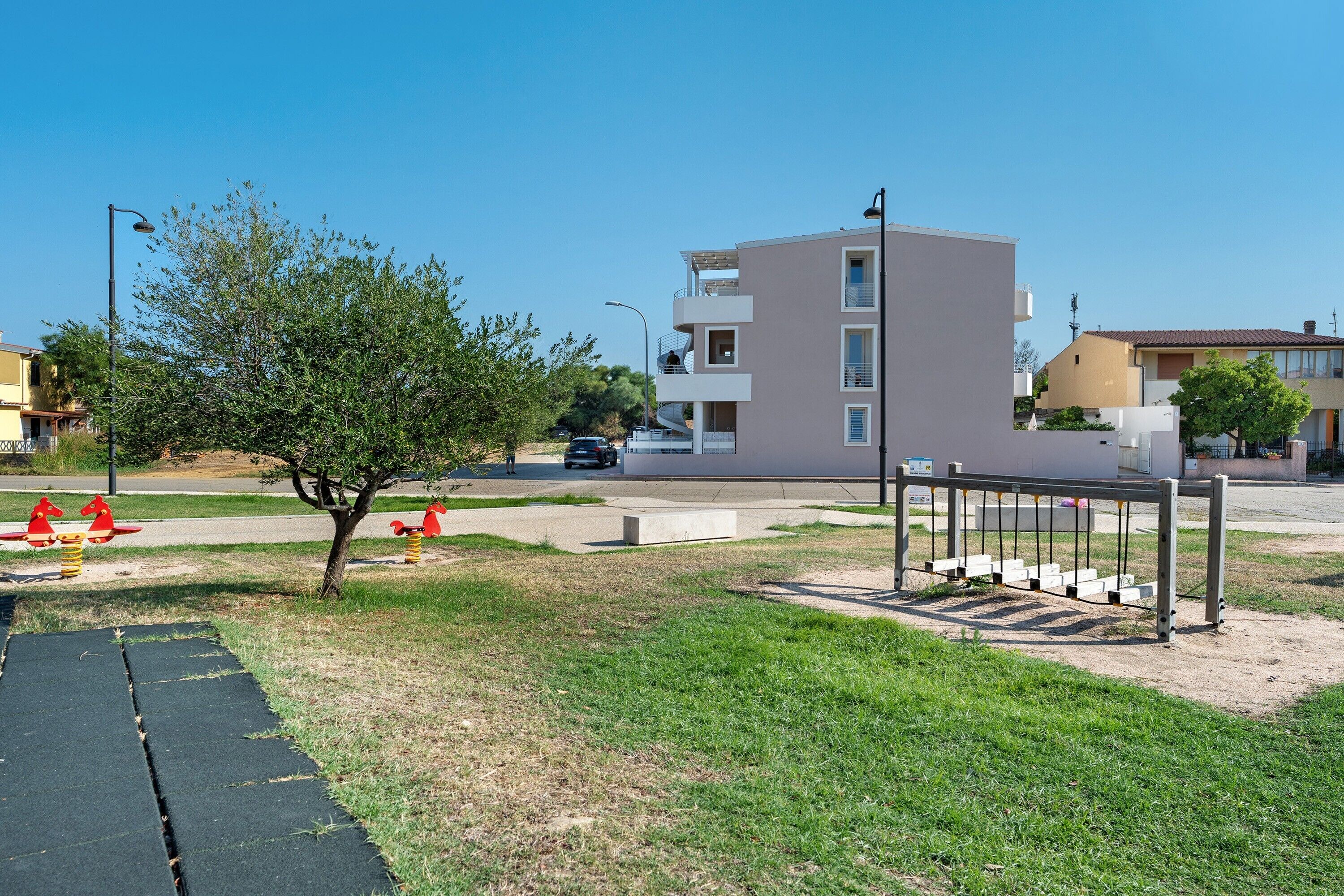 Un quartier résidentiel avec un immeuble moderne à deux étages, une aire de jeux dotée de balançoires et un arbre au premier plan.