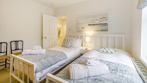 Hotelkamer met twee eenpersoonsbedden, een witte deur, een schilderij aan de muur en een tafeltje met een lamp.