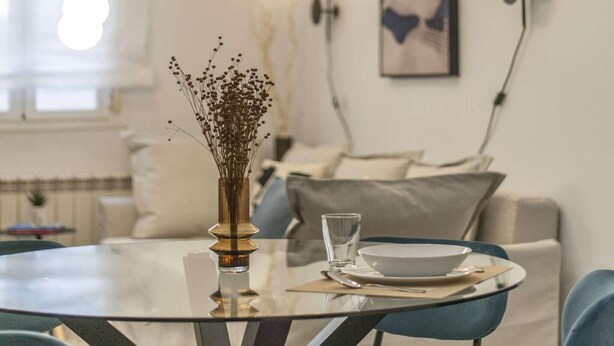 A dining area with a glass table, blue chairs, a vase with dried flowers, a bowl, and a glass of water. - Central Haven near Museums (Madrid)