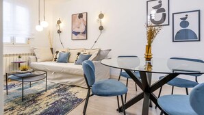 A modern living room with a sofa, a glass coffee table, and a round dining table with chairs. There are abstract wall art pieces and a vase with dried flowers. - Central Haven near Museums (Madrid)